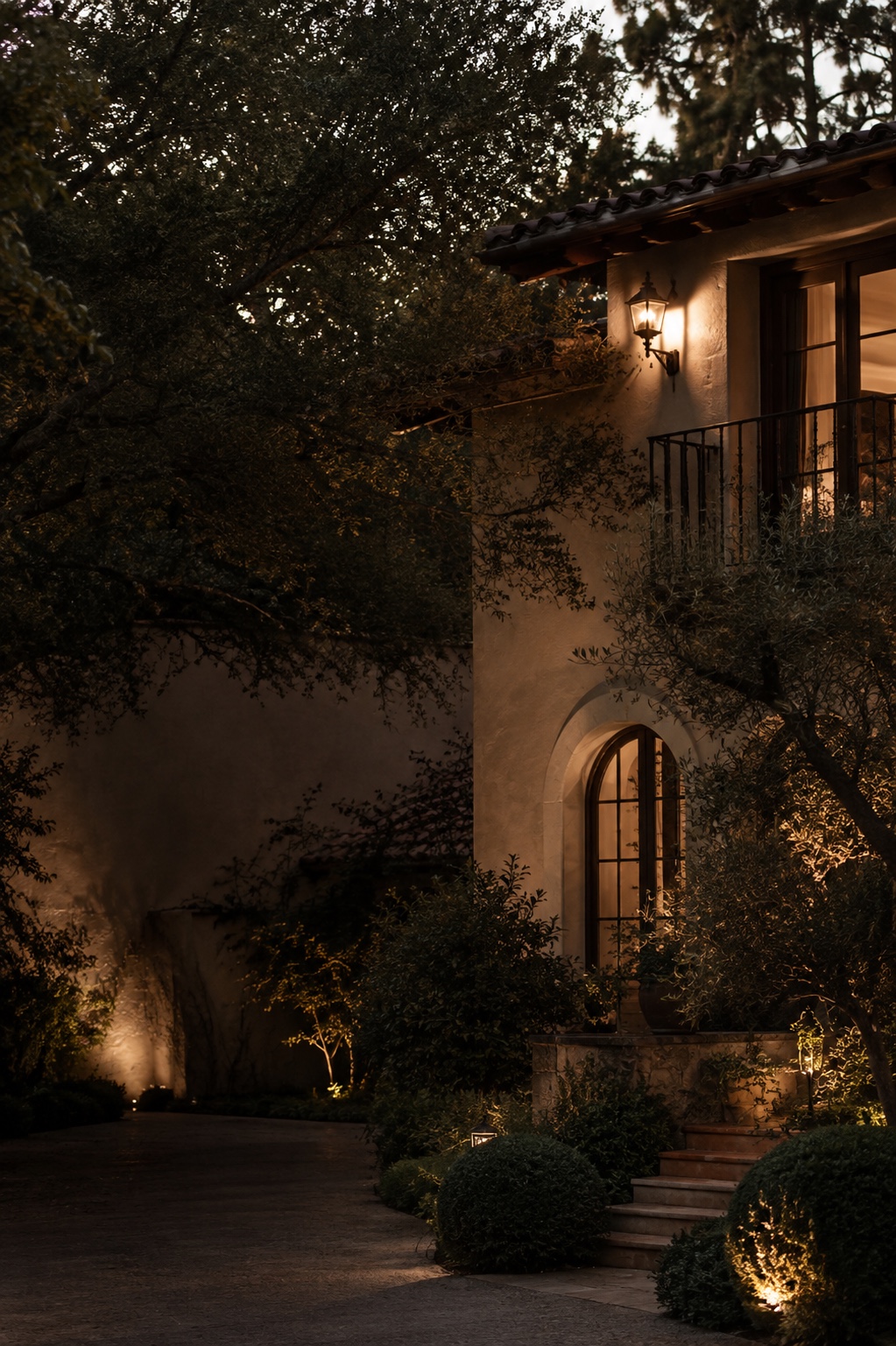 Warmly illuminated San Marino-style residence framed by mature trees at dusk